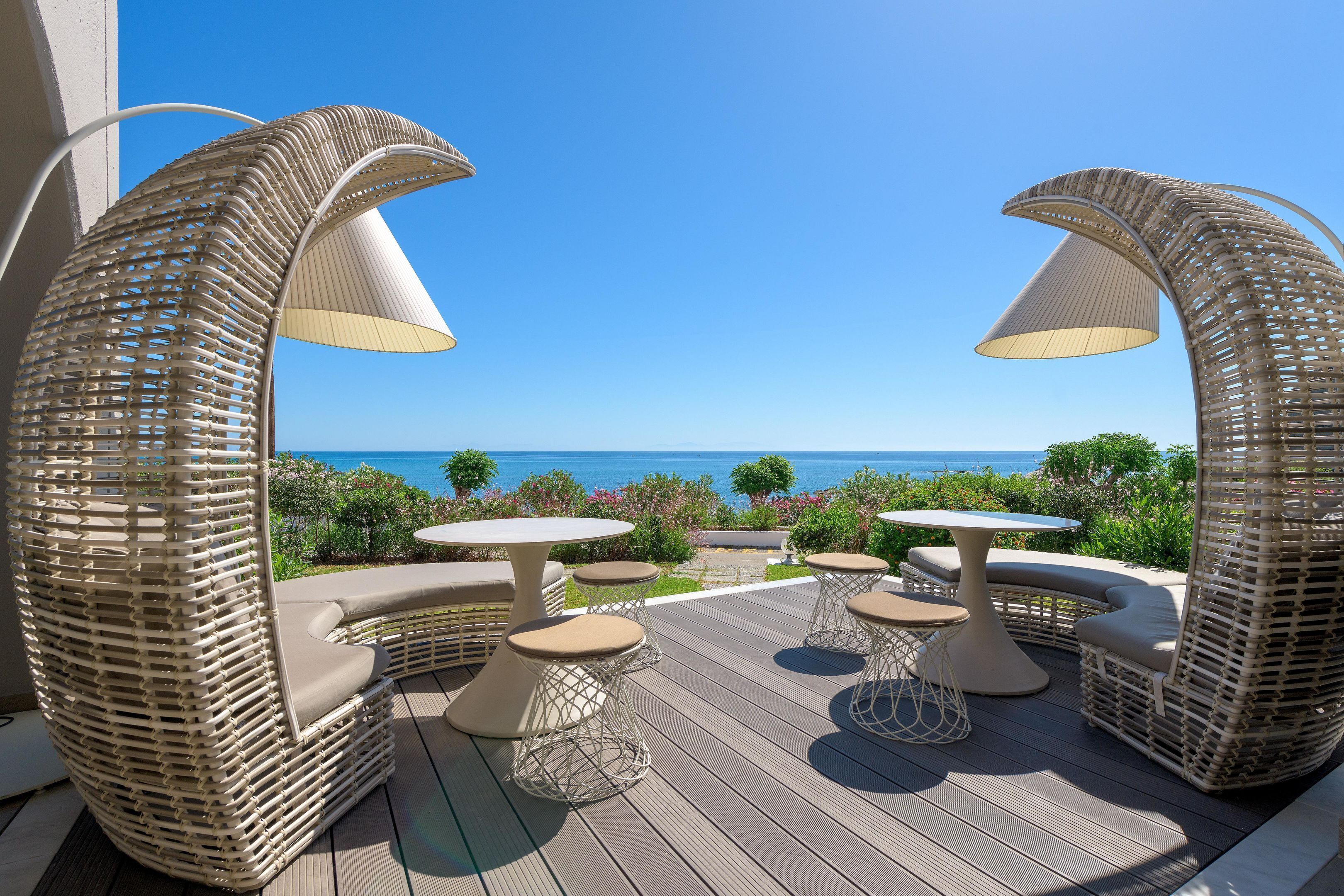 A deck with wicker furniture, including chairs and tables, overlooking a scenic view.