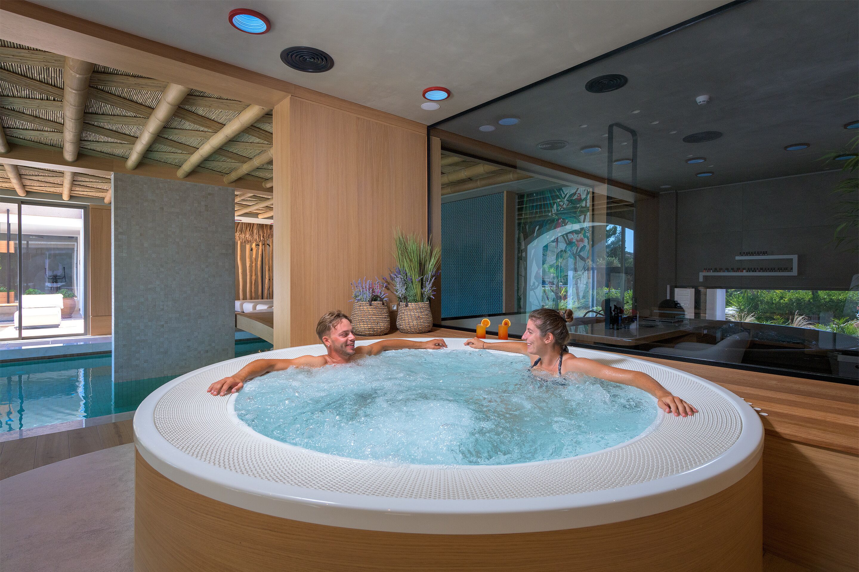 Una piscina interior moderna con jacuzzi, techo de madera y grandes ventanales.