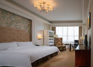 A hotel room with a large bed, a chandelier, a desk with a chair, and a television.
