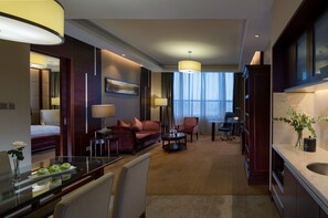 A hotel room with a bed, a sofa, a dining table, a kitchen area, and a view of the outdoors. - Venus Royal Hotel (Shenzhen)