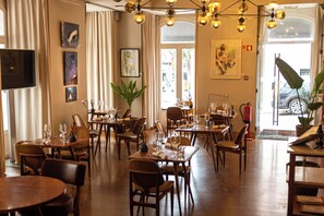 Et restaurantinteriør med flere spiseborde, stole og hængende, runde lysarmaturer.