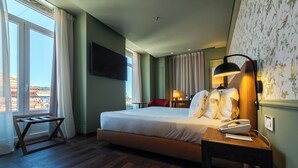 Een hotelkamer met een bed, nachtkastje, lamp en een aan de muur bevestigde televisie.