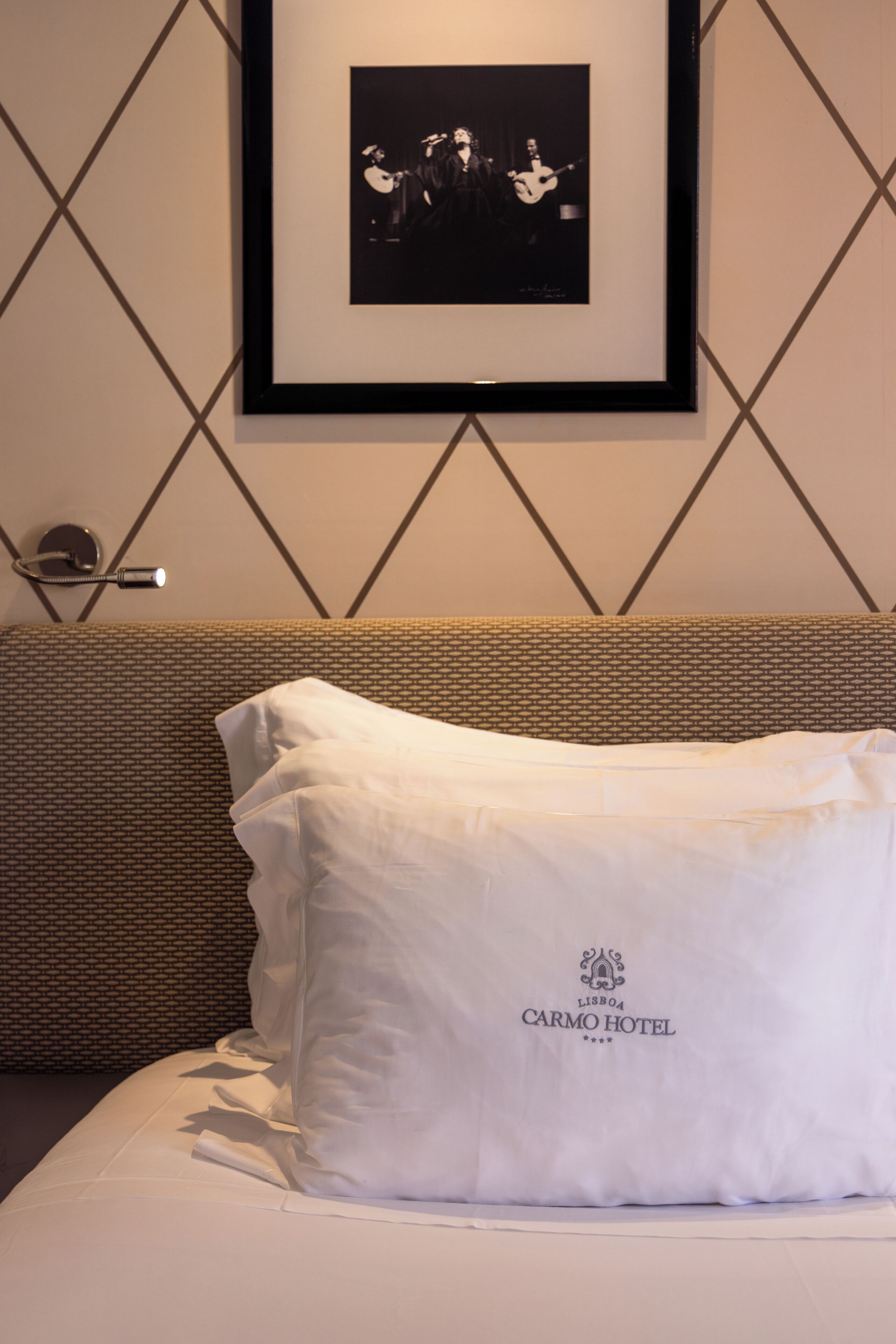 Une chambre d’hôtel avec une photographie en noir et blanc encadrée au mur, un lit avec une literie blanche et une tête de lit texturée.