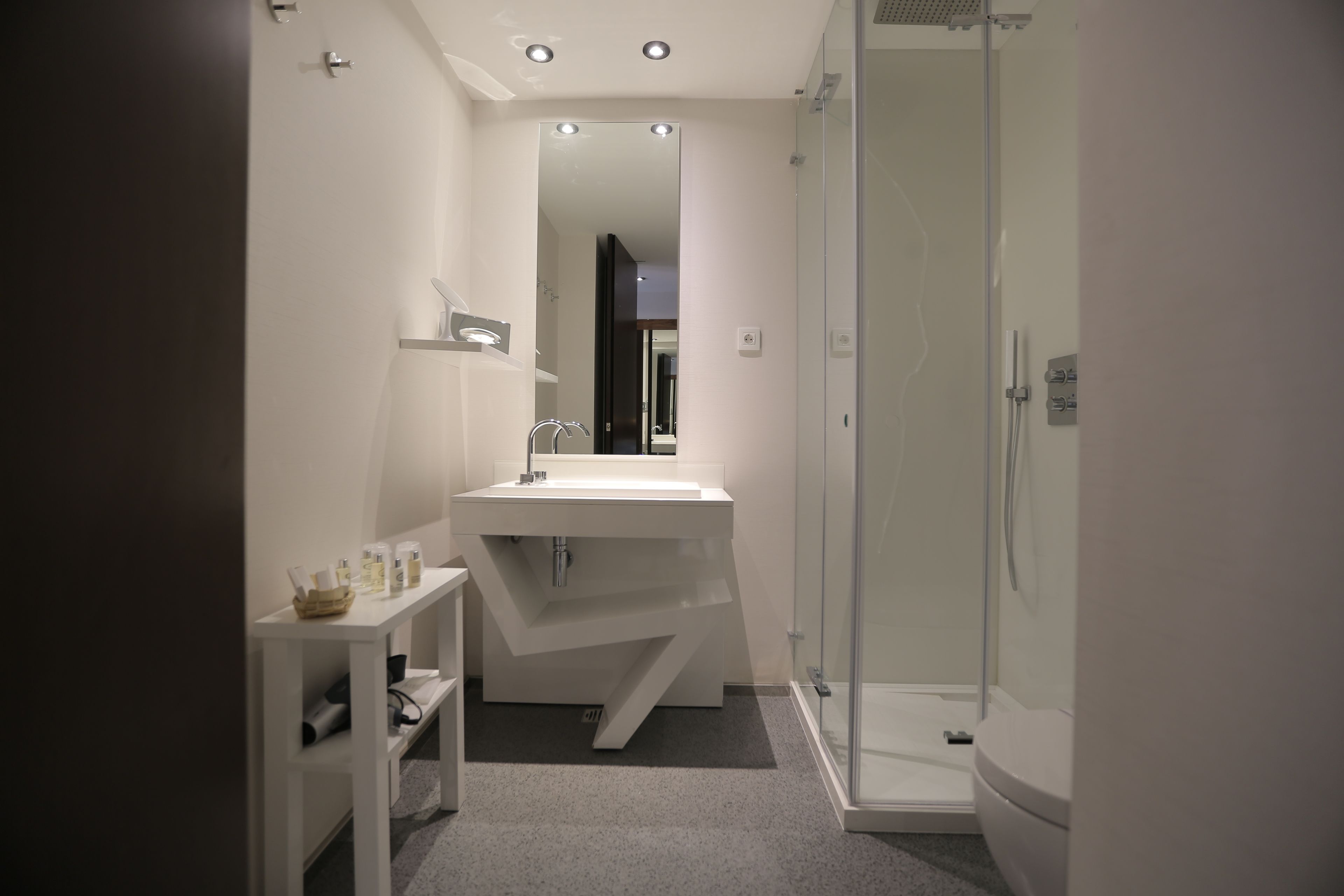 Un baño moderno con un lavamanos, espejo y ducha blancos.