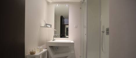Un baño moderno con un lavamanos, espejo y ducha blancos.