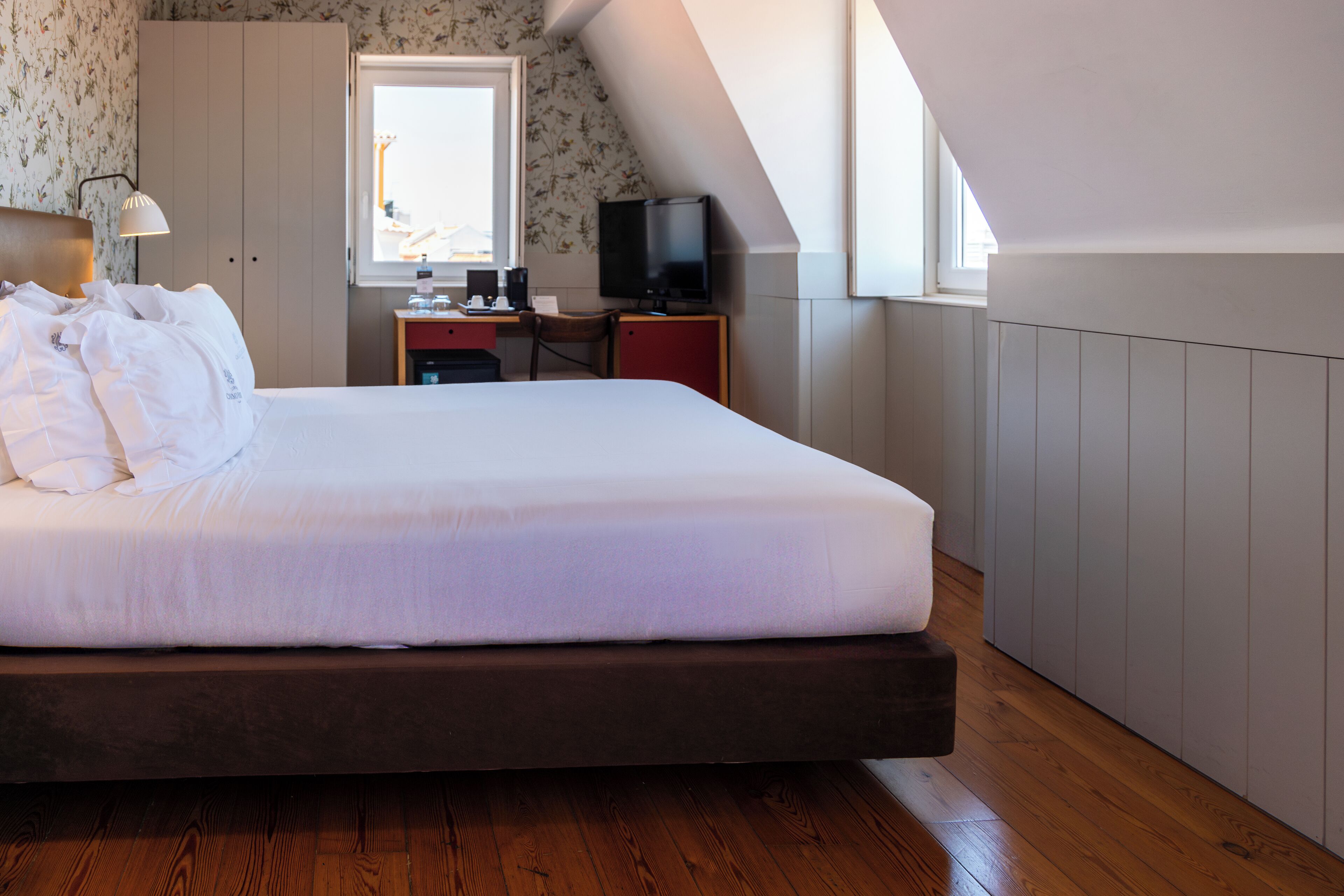 Une chambre avec un grand lit, un bureau avec un ordinateur et une télévision, une fenêtre et une armoire.