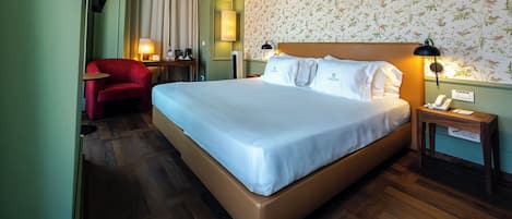 Habitación de hotel con una cama grande, un escritorio con silla, un teléfono y una lámpara.