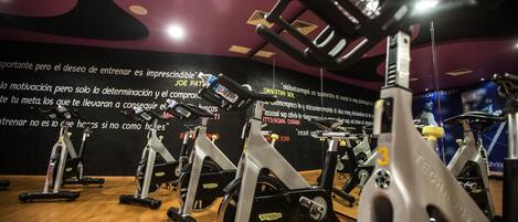A gym with stationary bikes, wooden flooring, and motivational posters on the walls.