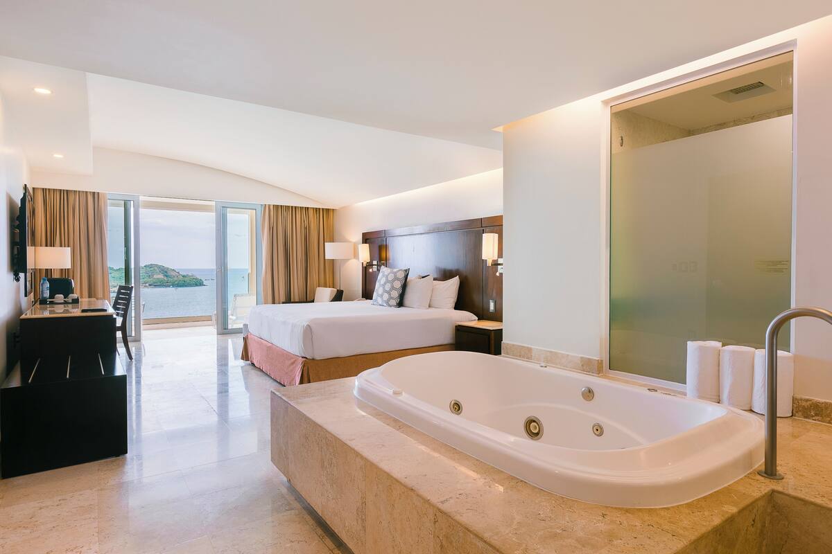 Habitación de hotel con una cama grande, un escritorio independiente con una silla, una bañera y vistas al mar.