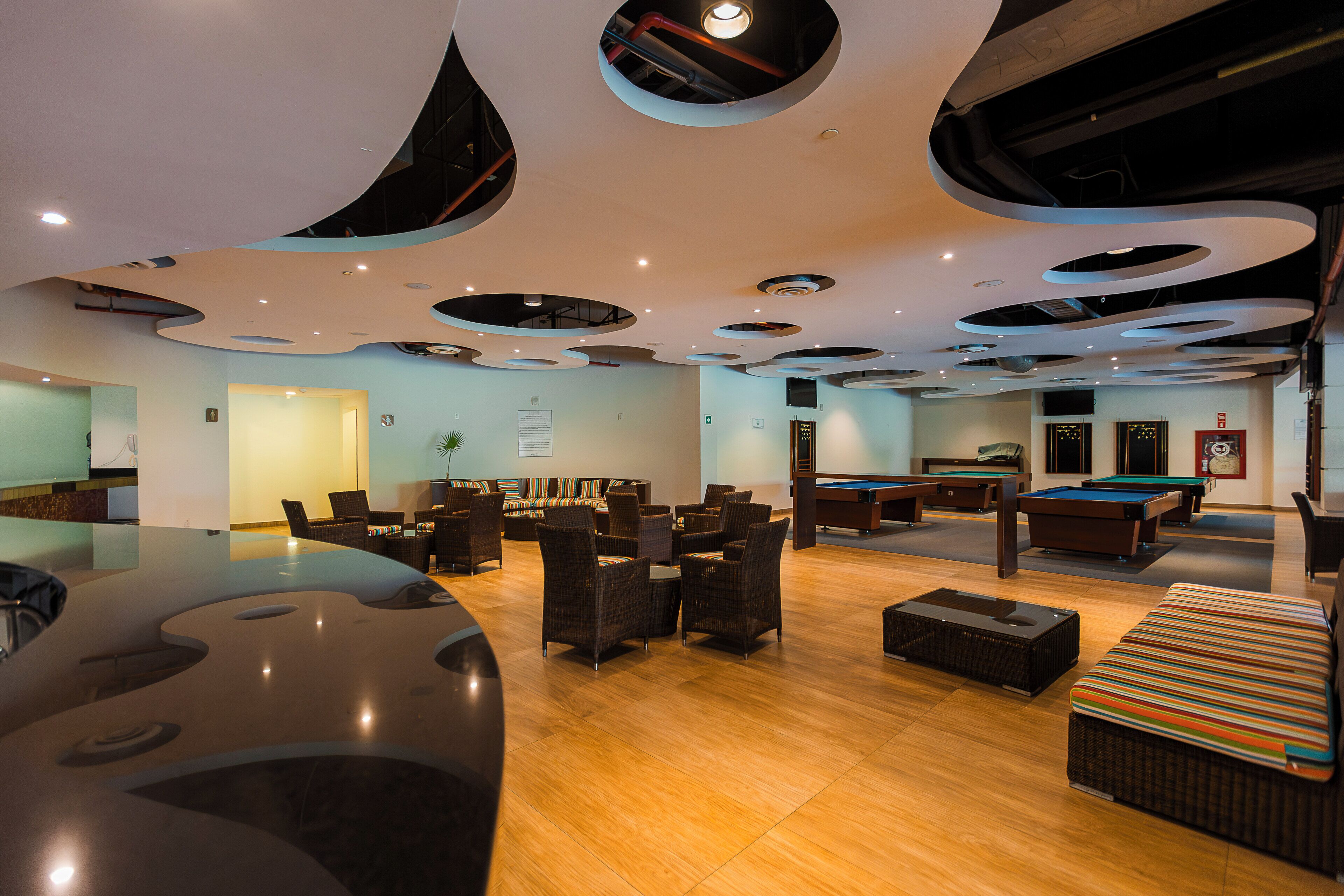 A modern lounge with a pool table, comfortable seating, and a unique ceiling design.