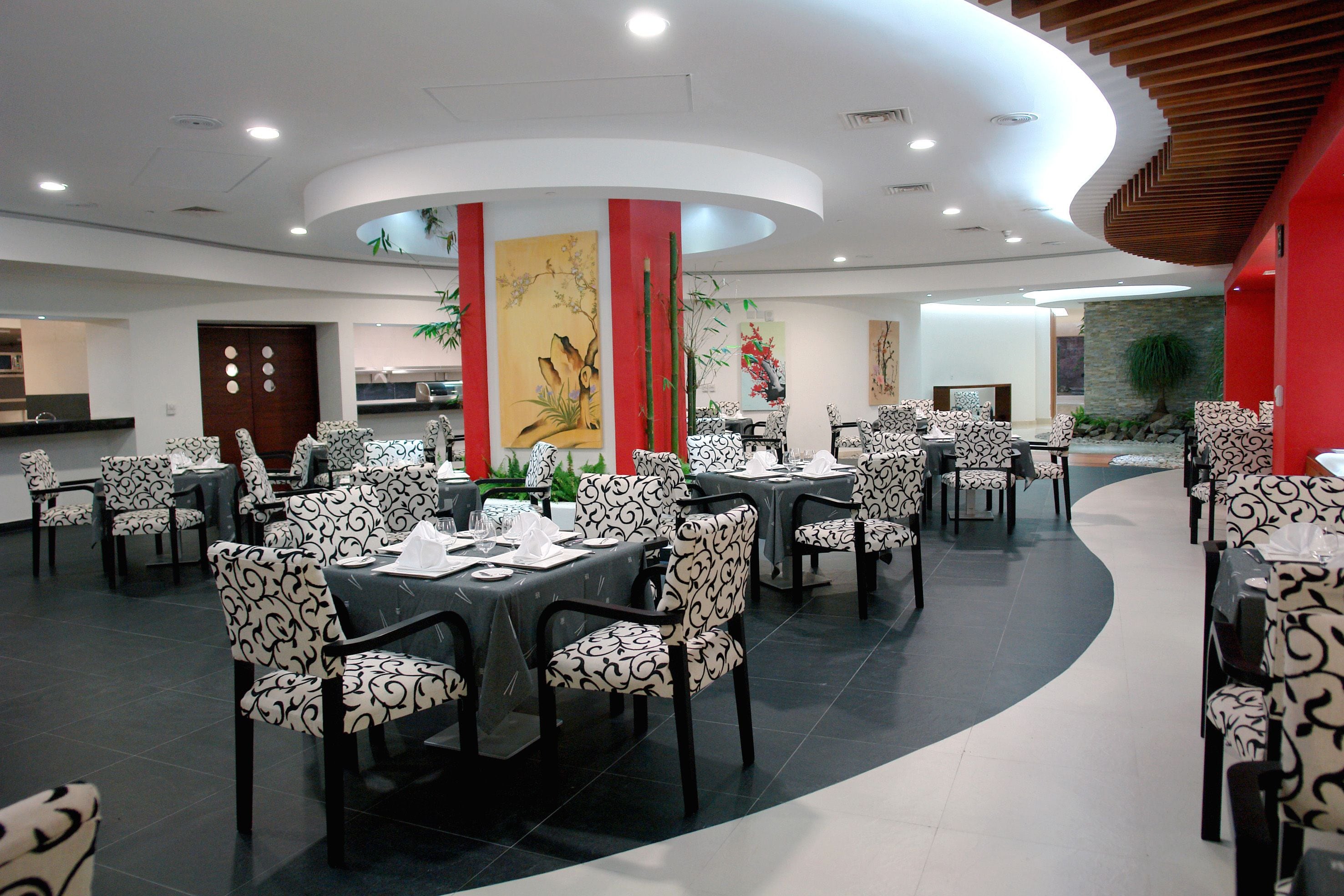 Un restaurante con mesas redondas, sillas estampadas, techo curvo y decoración en las paredes.