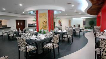 Un restaurante con mesas redondas, sillas estampadas, techo curvo y decoración en las paredes.