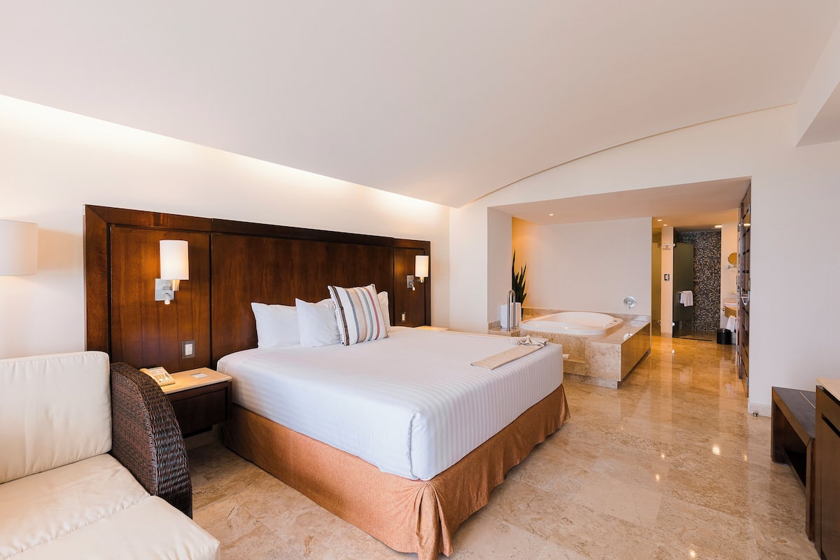 Una habitación de hotel moderna con una cama grande, un espacio de descanso, un baño con bañera y piso de mármol.