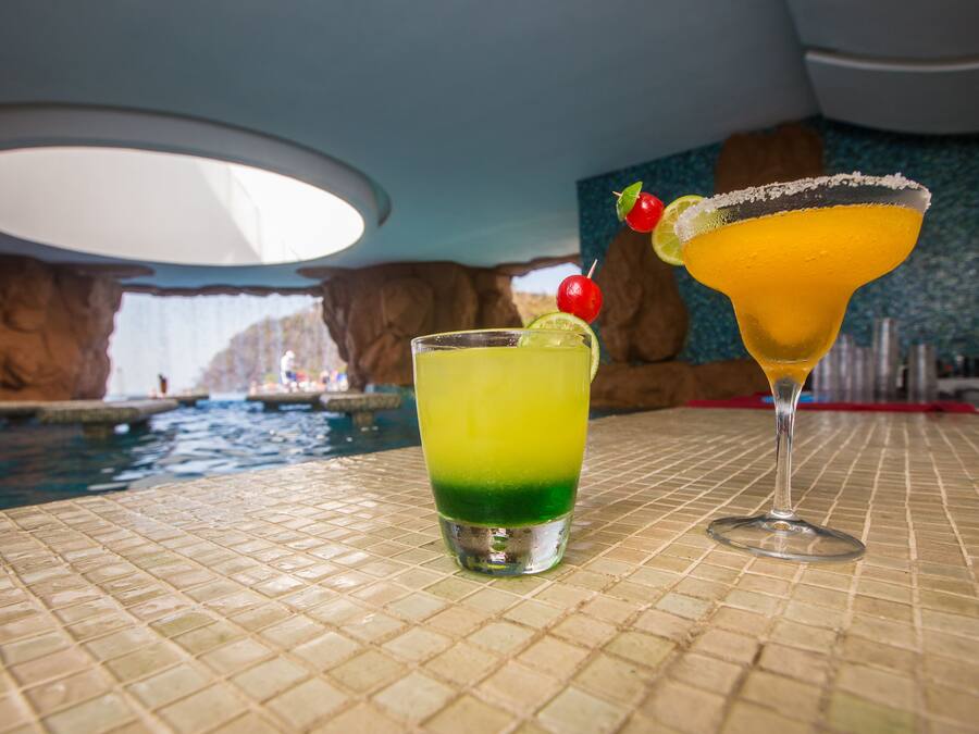 Two cocktails on a tiled table with a pool in the background.
