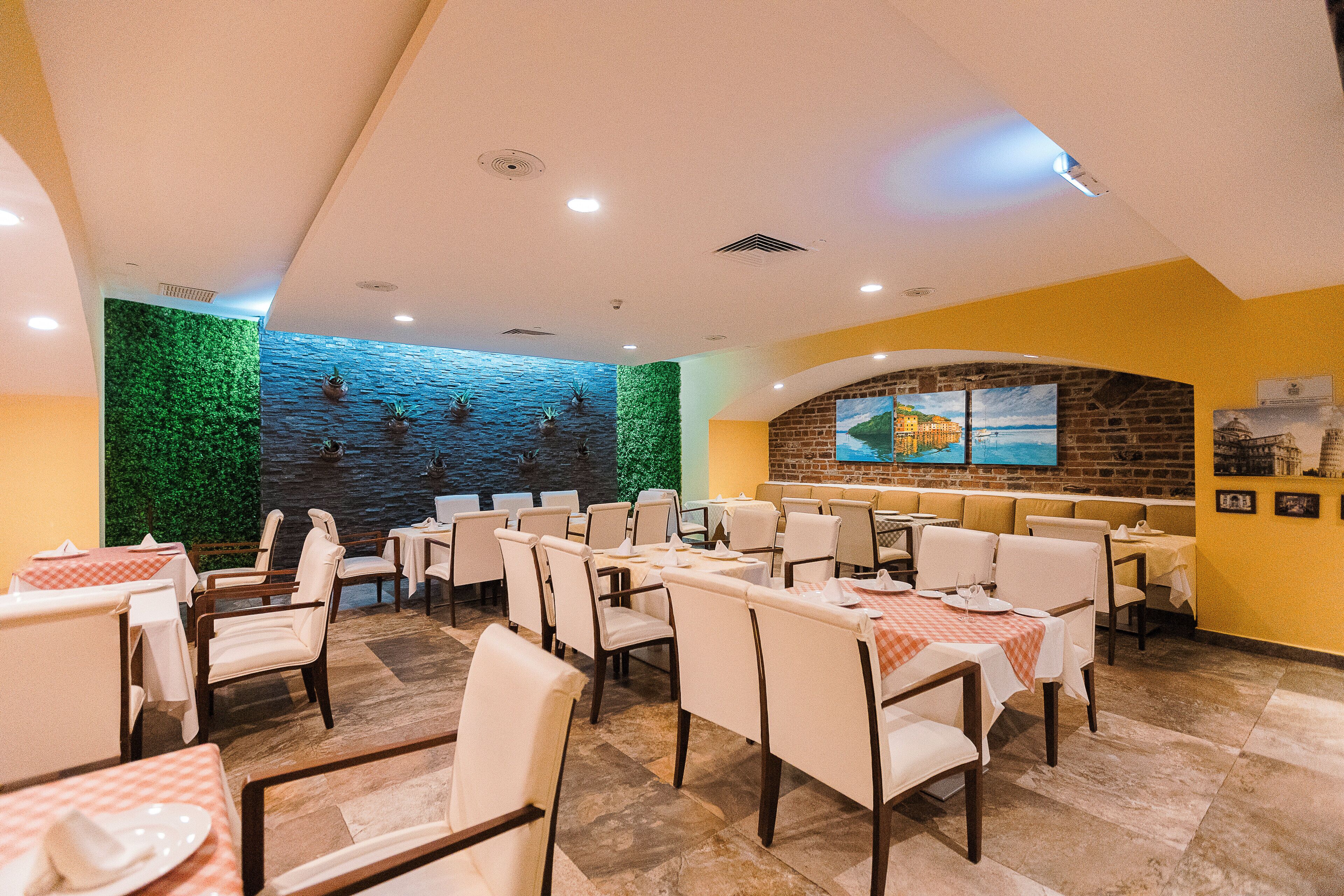 Un restaurant avec plusieurs tables et chaises, un mur végétal orné de plantes et un mur de briques sur lequel est accrochée une peinture.
