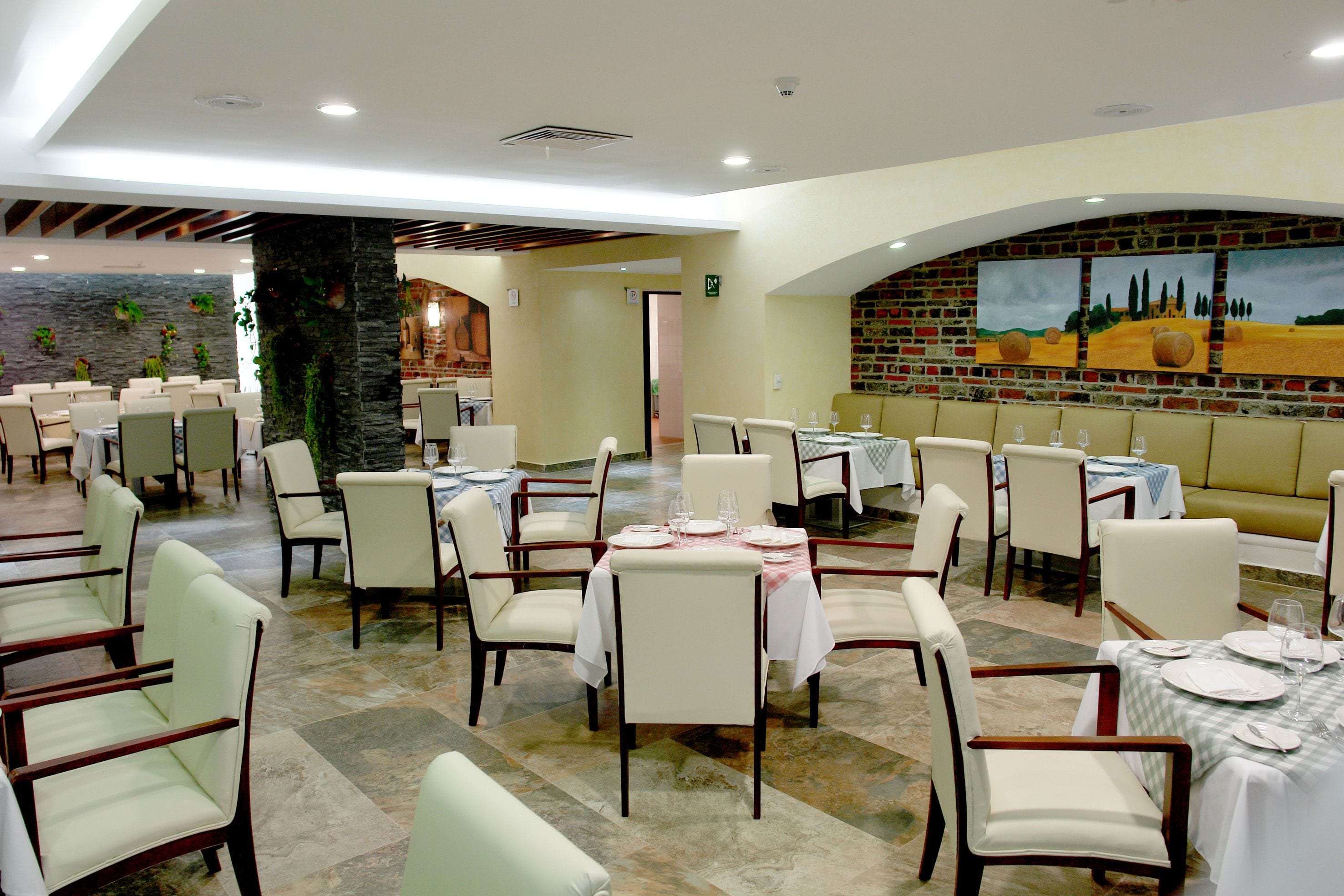 Un restaurante con varias mesas y sillas, una pared de ladrillo con pinturas y un pilar de piedra.