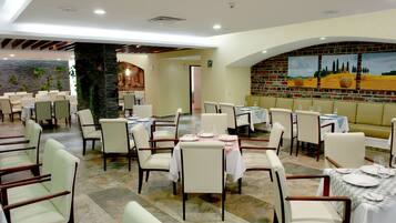 Un restaurante con varias mesas y sillas, una pared de ladrillo con pinturas y un pilar de piedra.