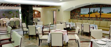 Un restaurante con varias mesas y sillas, una pared de ladrillo con pinturas y un pilar de piedra.