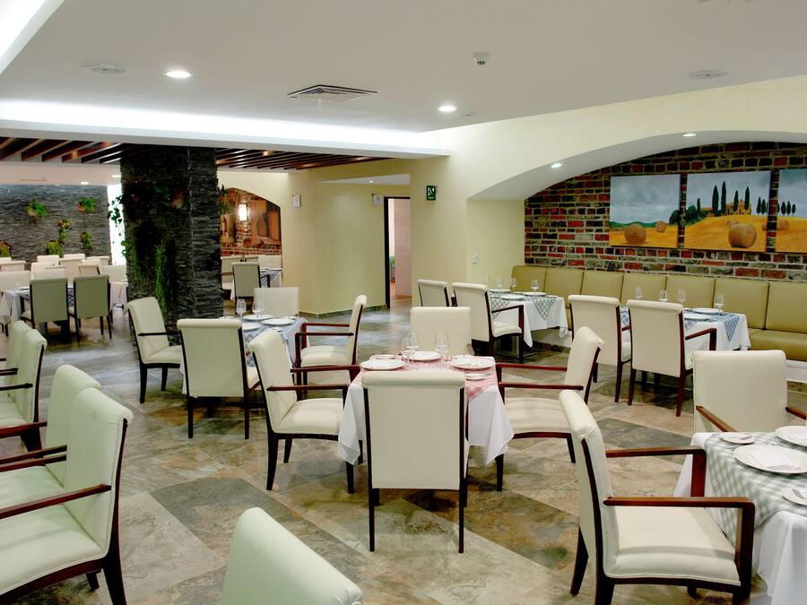 Un restaurante con varias mesas y sillas, una pared de ladrillo con pinturas y un pilar de piedra.