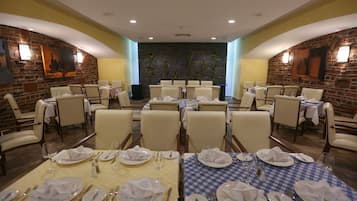 Un restaurant doté de nombreuses tables dressées pour le service, avec un mur en briques et des œuvres d’art encadrées.