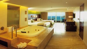 Une chambre d’hôtel avec une grande baignoire, deux lits, un balcon avec vue sur la mer et un bureau avec une lampe.