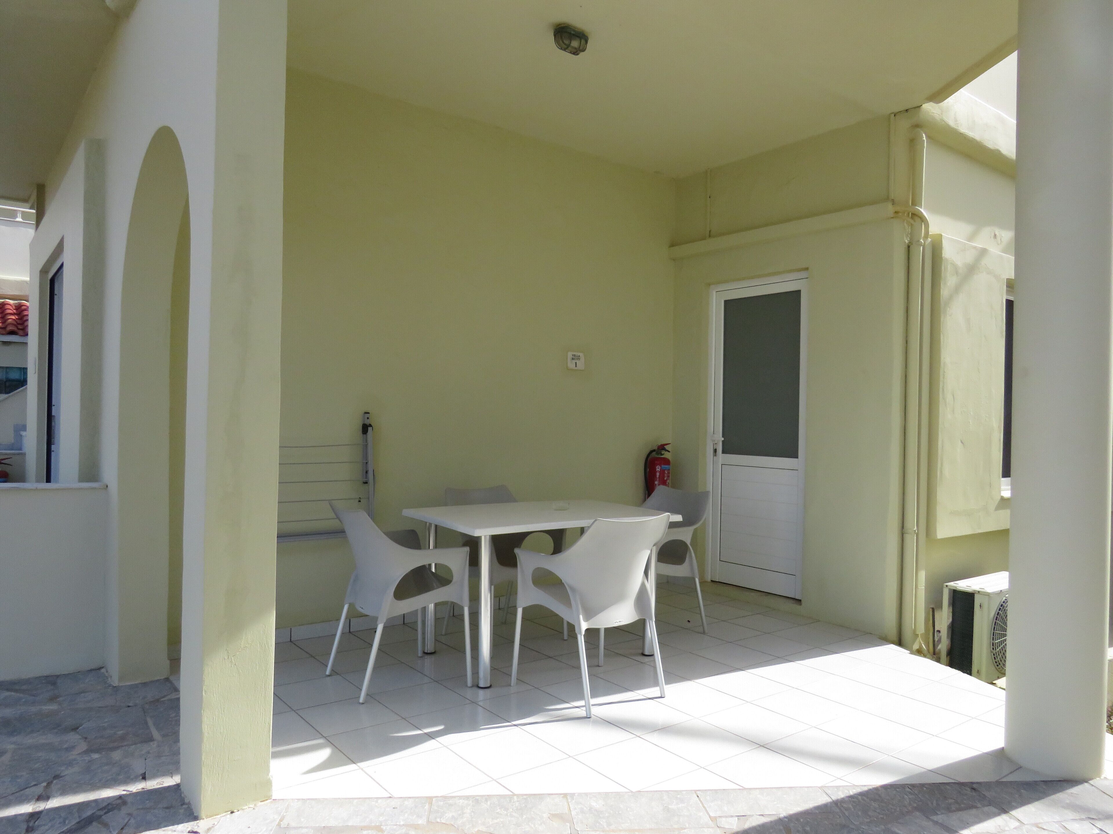A room with a white table and chairs, a door, and a window.