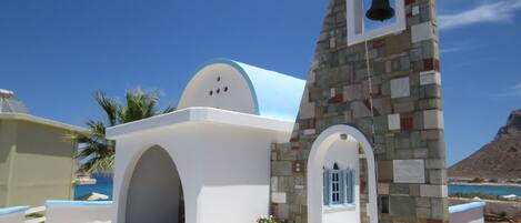 A white building with a bell tower, a stone wall, and a tiled floor.