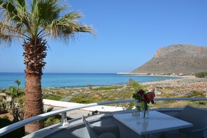 Une terrasse avec vue sur la mer, un palmier et une table agrémentée d’un vase de fleurs.