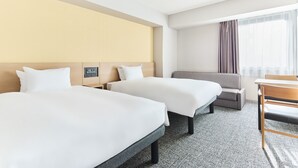 Ein Hotelzimmer mit zwei Betten, einem Sofa, einem Schreibtisch und einem Fenster mit Vorhängen.