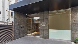 Ein moderner Gebäudeeingang mit Glastür, Metalltreppe und einem Schild mit der Aufschrift 'Sofitel Ersa Inn'.