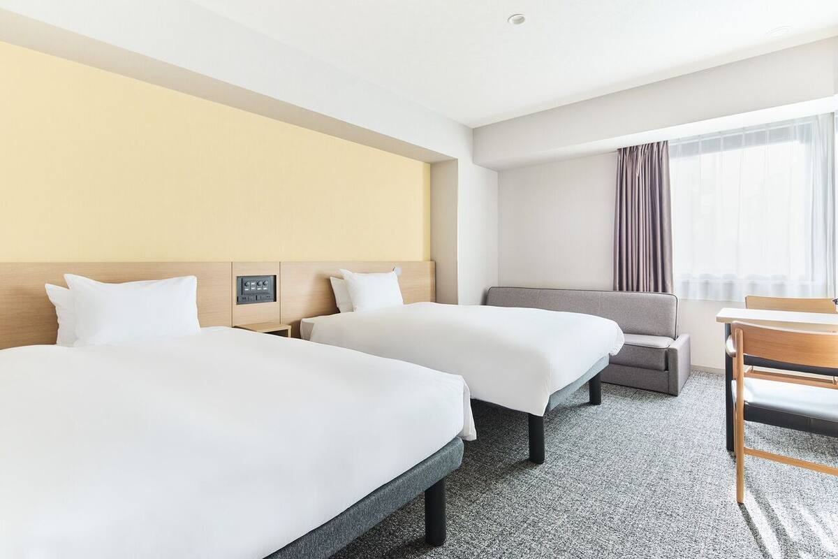 Ein Hotelzimmer mit zwei Betten, einem Sofa, einem Schreibtisch und einem Fenster mit Vorhängen.
