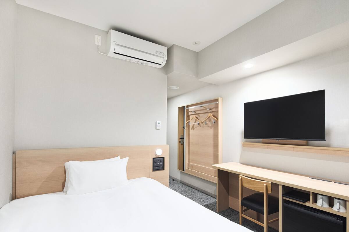 Ein Hotelzimmer mit Bett, Schreibtisch, Fernseher, Klimaanlage und Kleiderschrank.