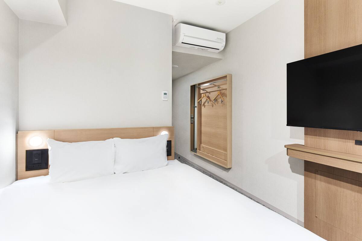 Ein Hotelzimmer mit Bett, Fernseher, Holzschrank und Wandklimaanlage.