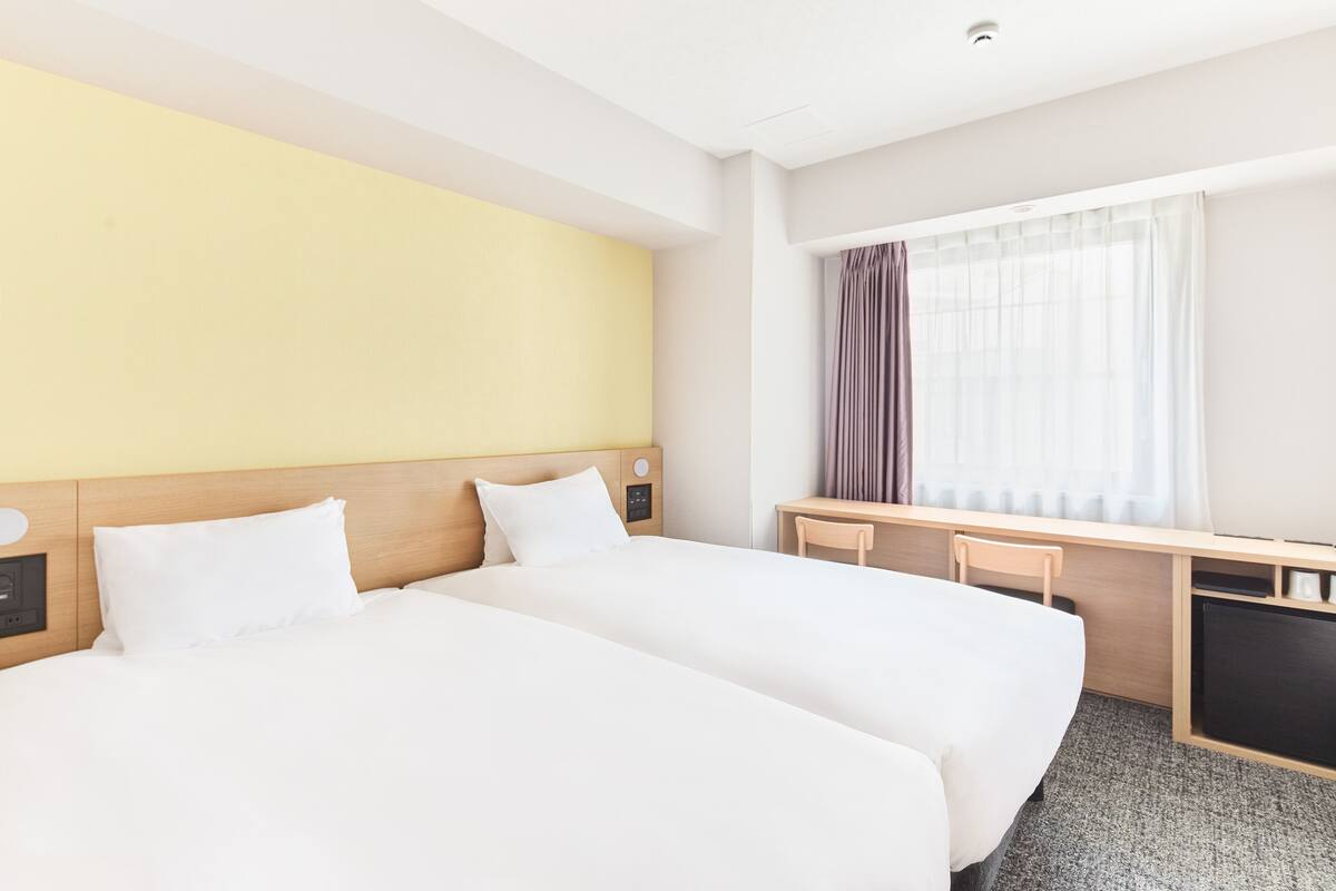 Ein Hotelzimmer mit zwei Betten, einem Schreibtisch und einem Fenster mit Vorhängen.
