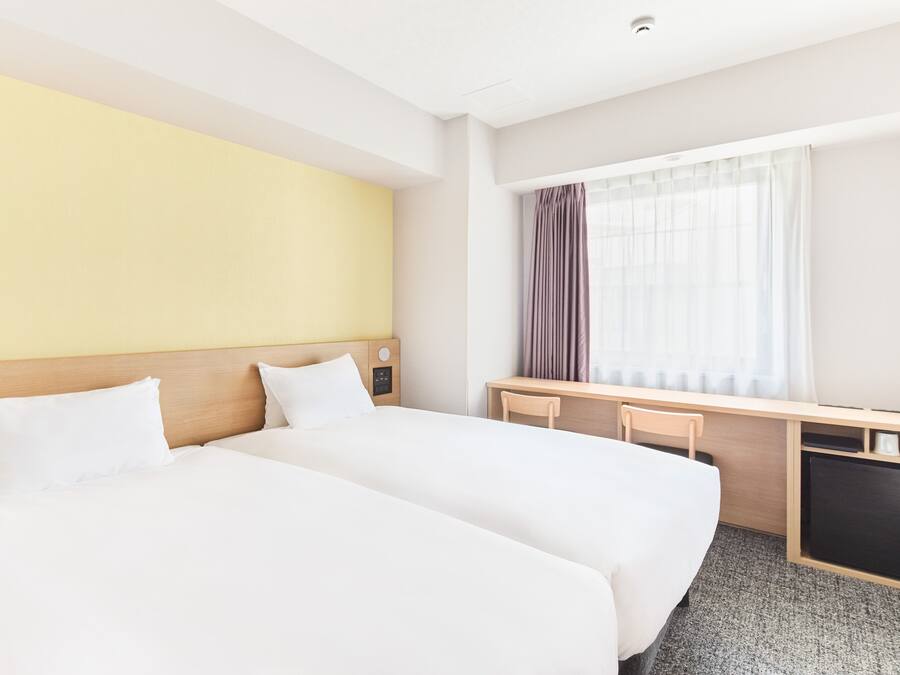 A hotel room with two beds, a desk, and a window with curtains.
