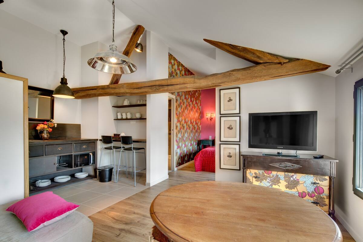 Una sala moderna con una mesa de comedor de madera, un televisor y una cocina con horno empotrado.