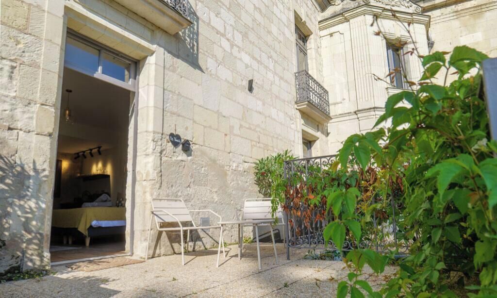 Un bâtiment en pierre doté d’un balcon, avec un lit visible à l’intérieur, et des sièges à l’extérieur.