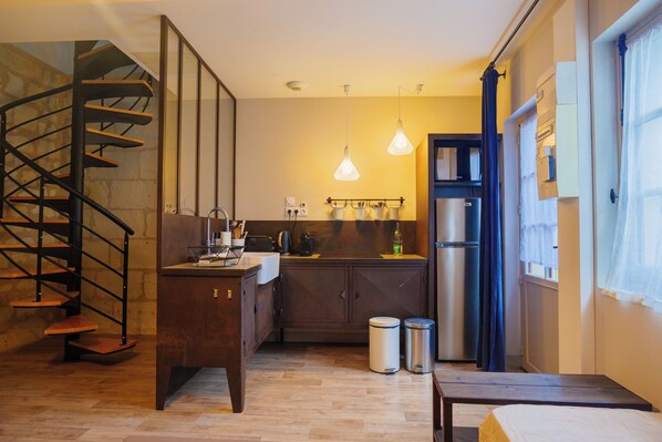 A compact kitchen with a built-in stove, a sink, and a refrigerator. There is a wooden staircase leading to an upper level. - Château de Candes Art et Spa (Candes-Saint-Martin)