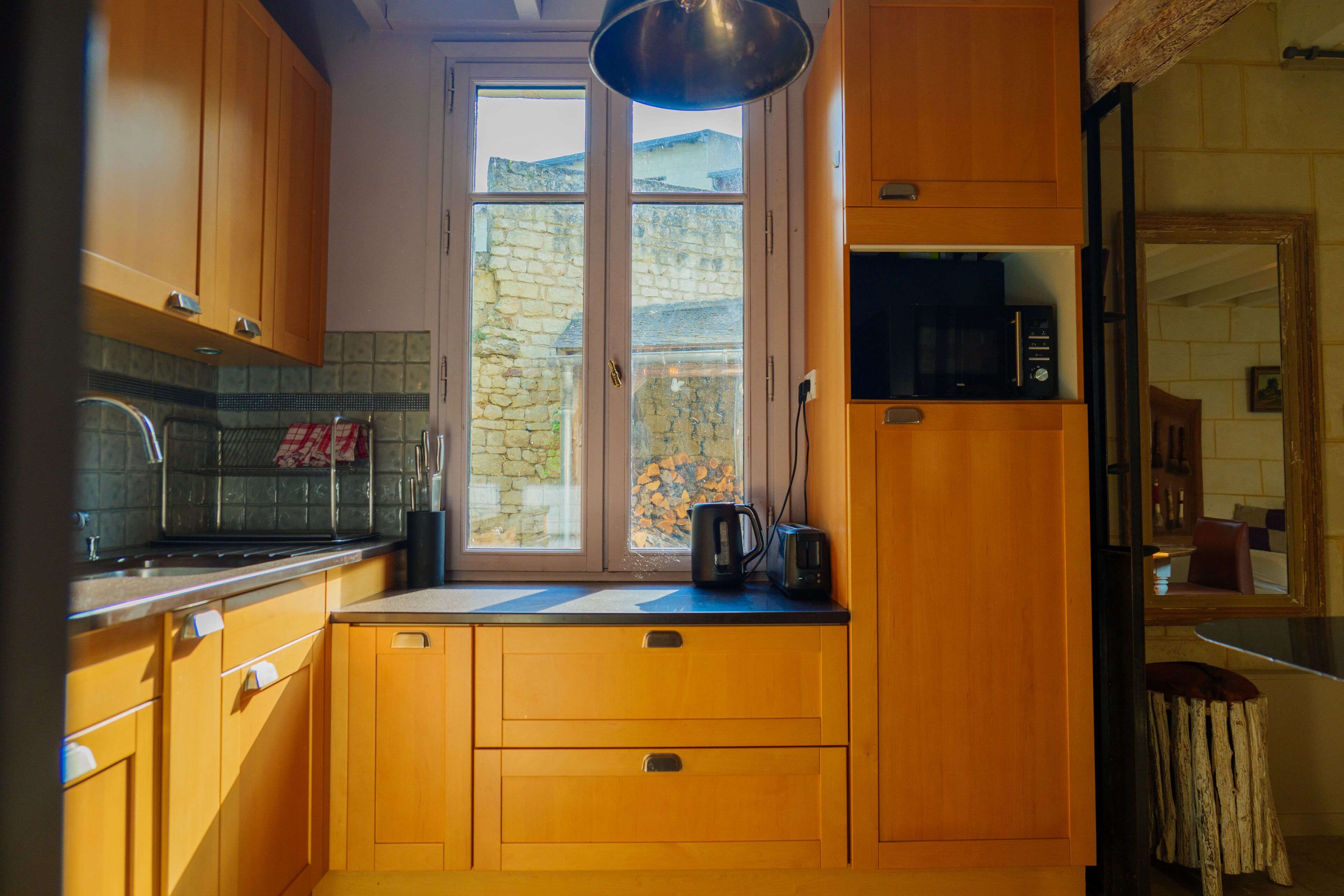 Una cocina con armarios de madera, una ventana con vista a un muro de piedra y un microondas en la encimera.