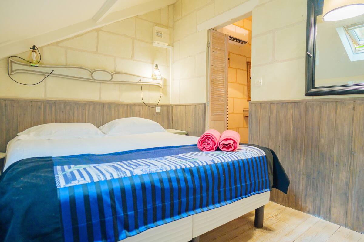 Una habitación de hotel con una cama, cabecera de madera, lámpara de pared y un espejo.