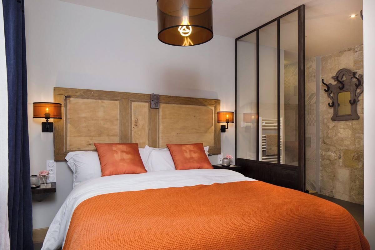 Habitación de hotel con una cama grande, dos lámparas de pared, un cabecero de madera y una pared de piedra.