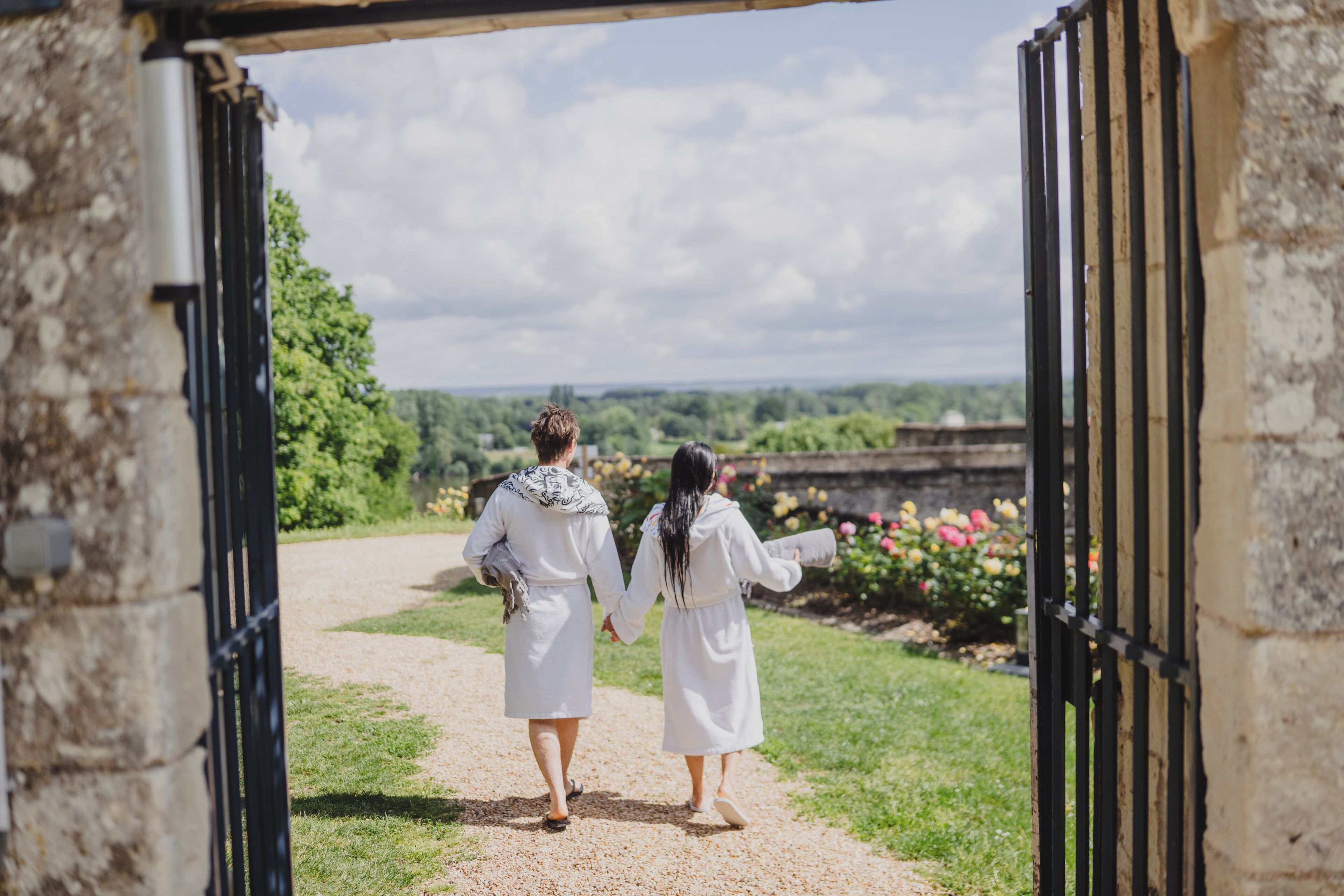 A pathway leading through an open gate, surrounded by greenery and a stone wall.