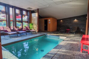 Zona de piscina con sillones de descanso, sauna de madera y vistas a zonas verdes.
