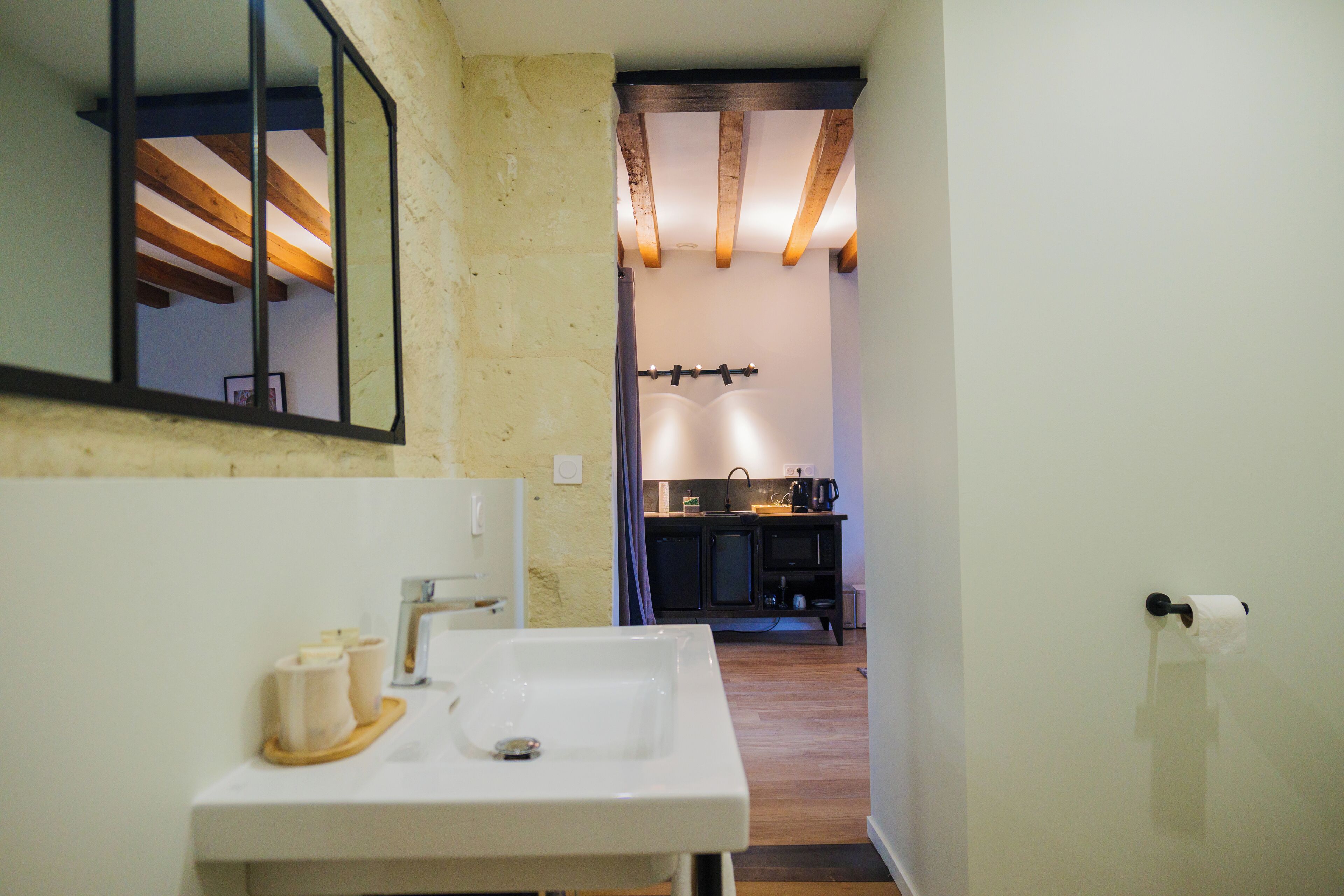 A bathroom with a sink, mirror, and wooden beams above the ceiling.