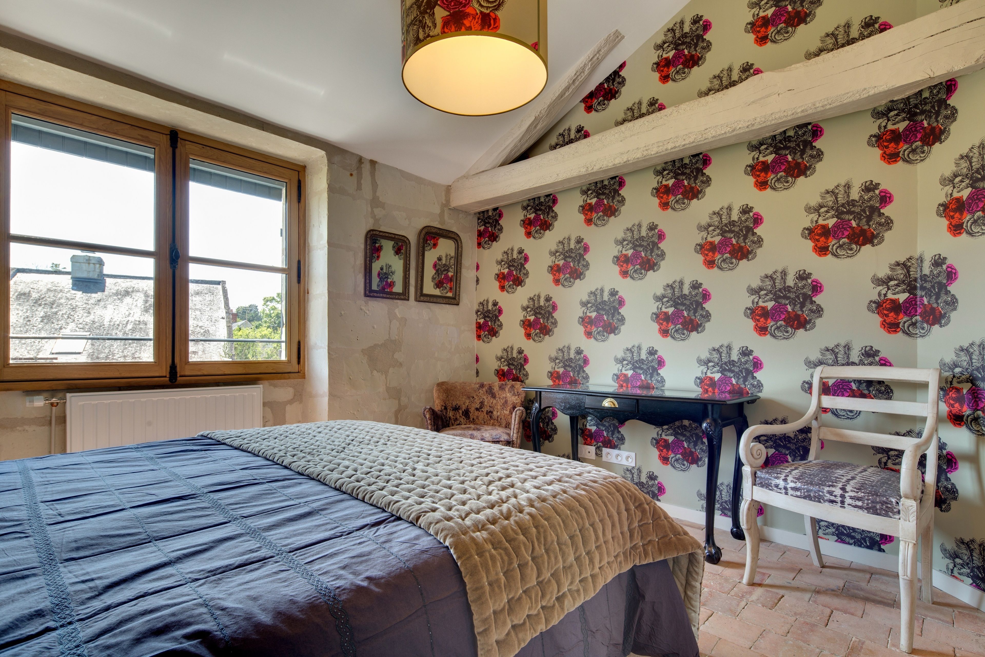 A bedroom with a large bed, a chair, a desk, and a window.