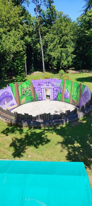 Un espacio circular al aire libre con suelo de arena, rodeado por una valla de madera decorada con murales de colores.