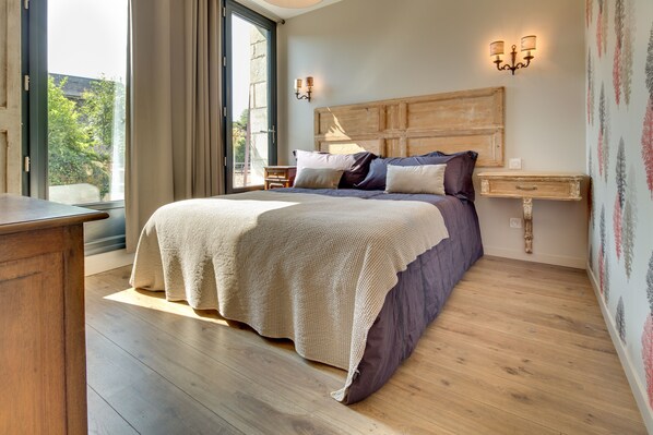 A bedroom with a large bed, wooden headboard, bedside table, and a window with curtains. - Château de Candes Art et Spa (Candes-Saint-Martin)