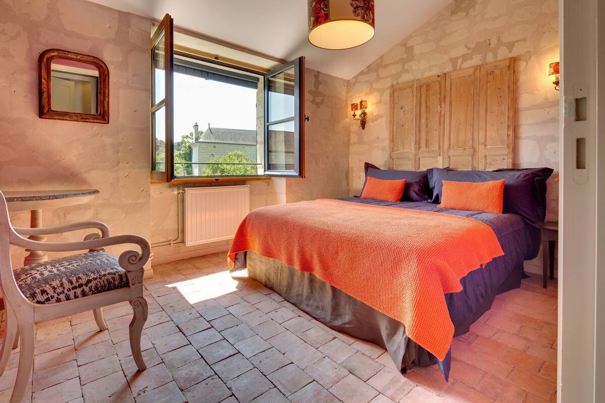 Un dormitorio con cama, una silla, un ventanal y un armario de madera.