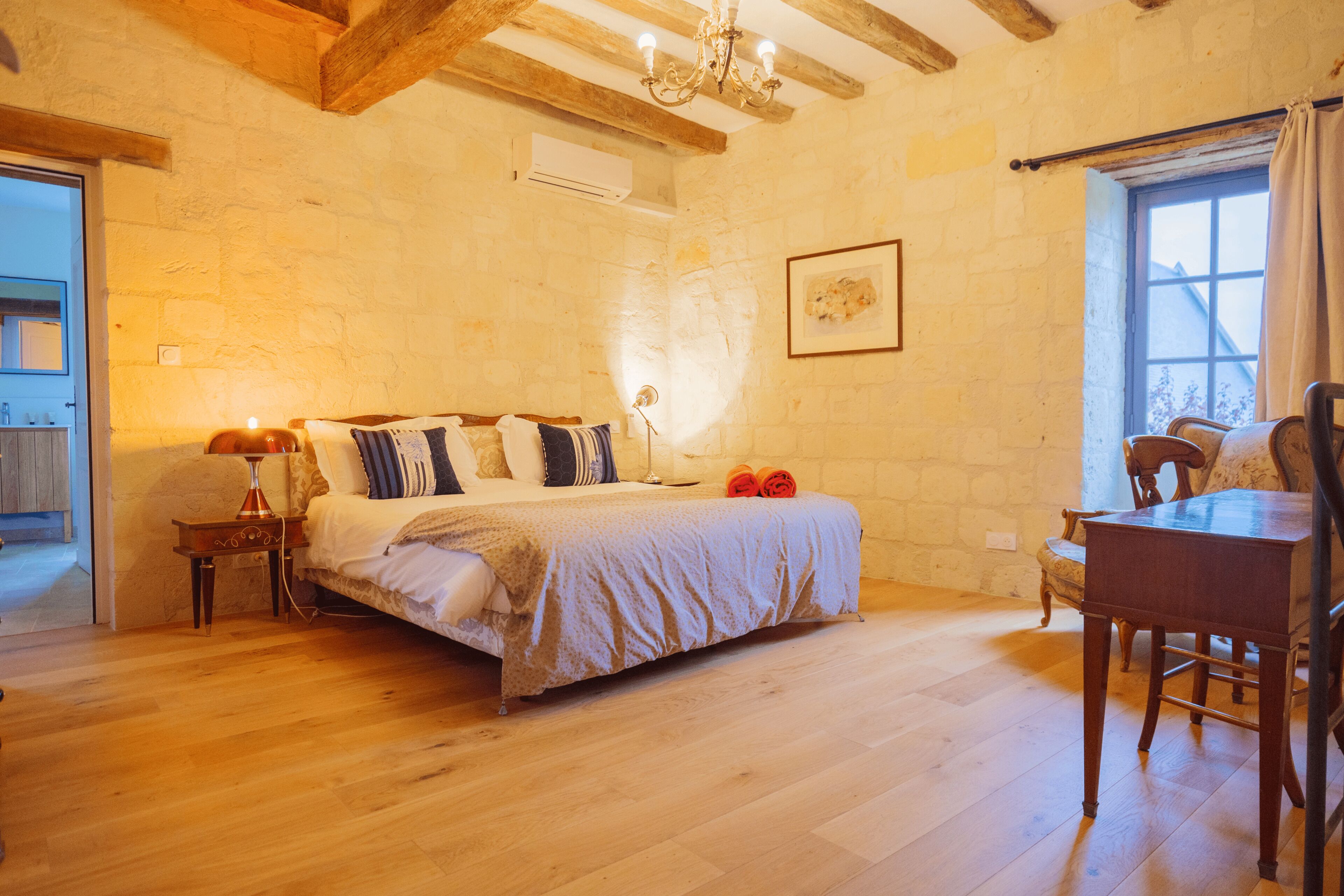 A bedroom with a wooden bed, a bedside table with a lamp, a chair, and a window with curtains.