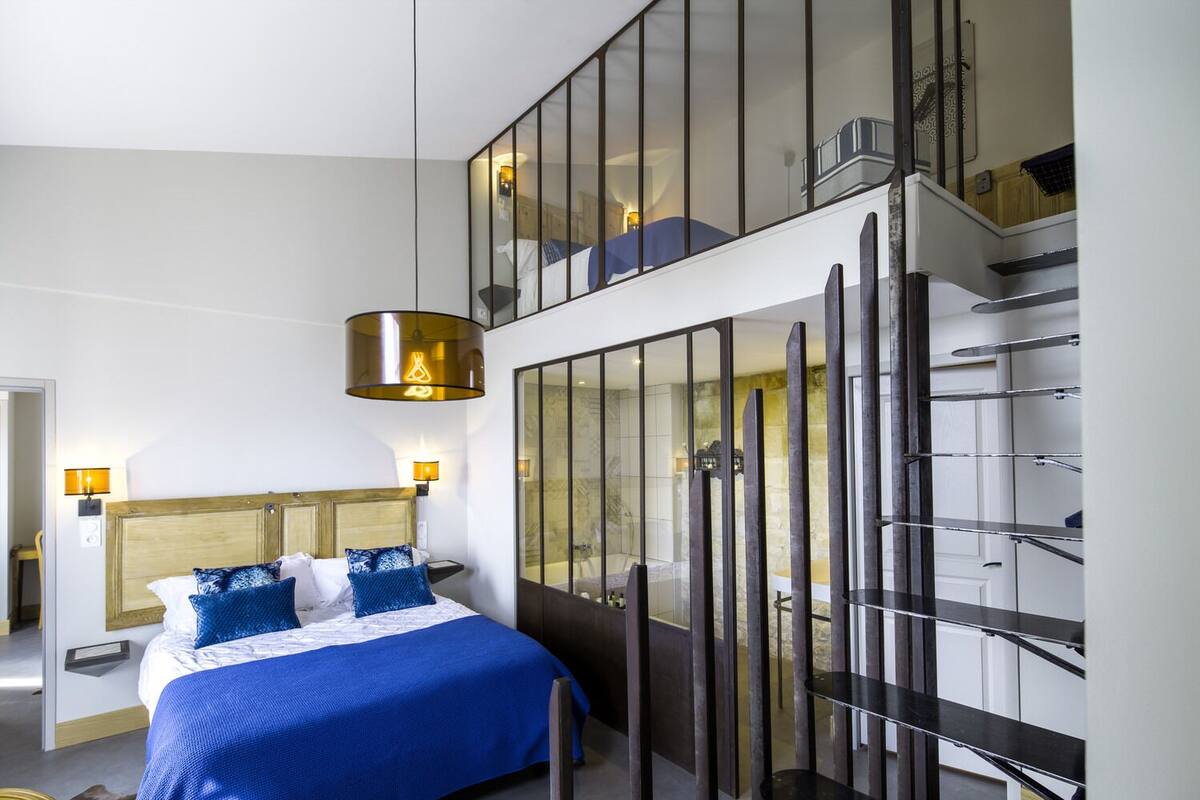 Una habitación de hotel moderna con una cama grande, un separador de vidrio y una escalera.